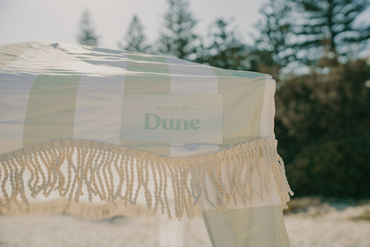 A serene beachside collage highlighting the Salted Sage Cabana, styled with soft green stripes, sandy tones, and relaxed coastal living.