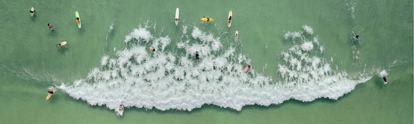 Aerial view of surfers paddling through turquoise waves along the Gold Coast shoreline, showcasing the beach lifestyle that inspires House of Dune.