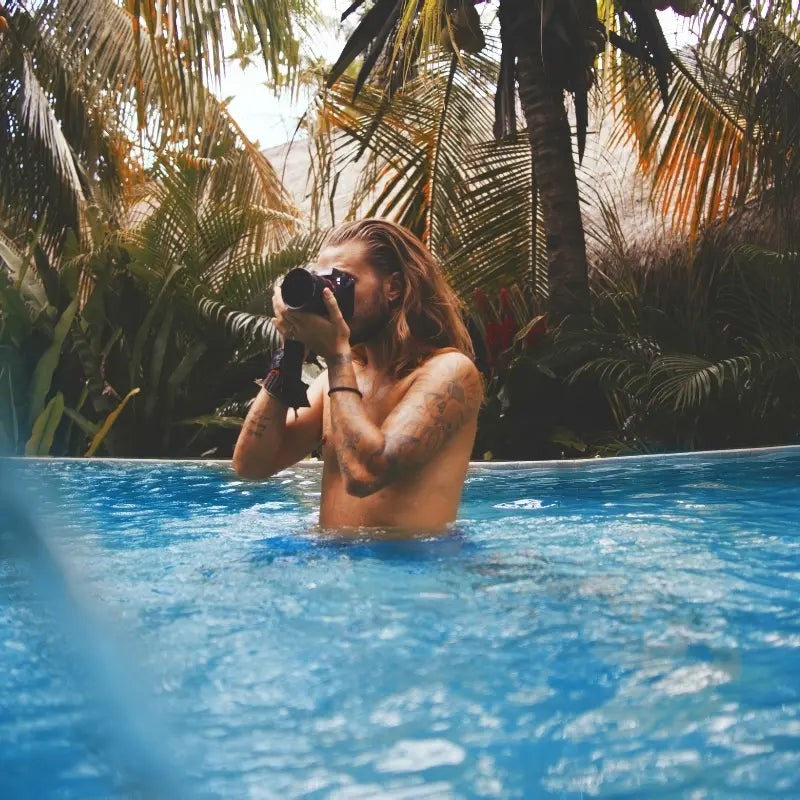 Male relaxing in a pool with palm trees in the background, lifestyle image for House of Dune media.