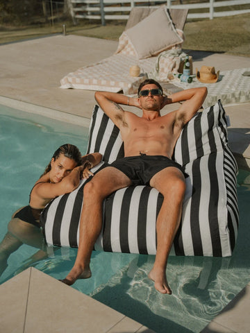 Man relaxing on the House of Dune Orca Stripe Floating Lounger beside the pool, showcasing the elegant monochrome design in a luxurious outdoor setting.