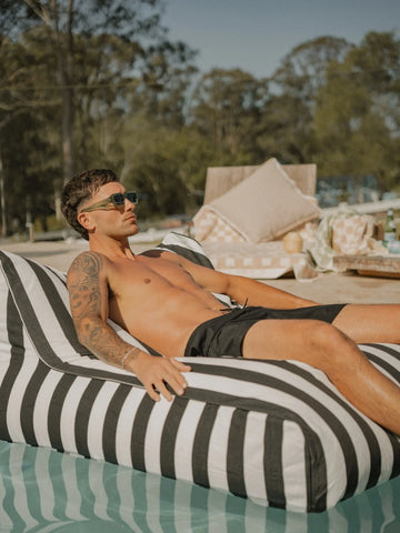 Man sunbathing on the House of Dune Orca Stripe Floating Lounger in a serene pool setting, designed for luxury and relaxation under the sun.