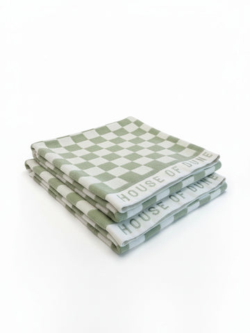 Set of two House of Dune Salted Sage beach towels with green and white checkerboard pattern neatly folded on a white surface.