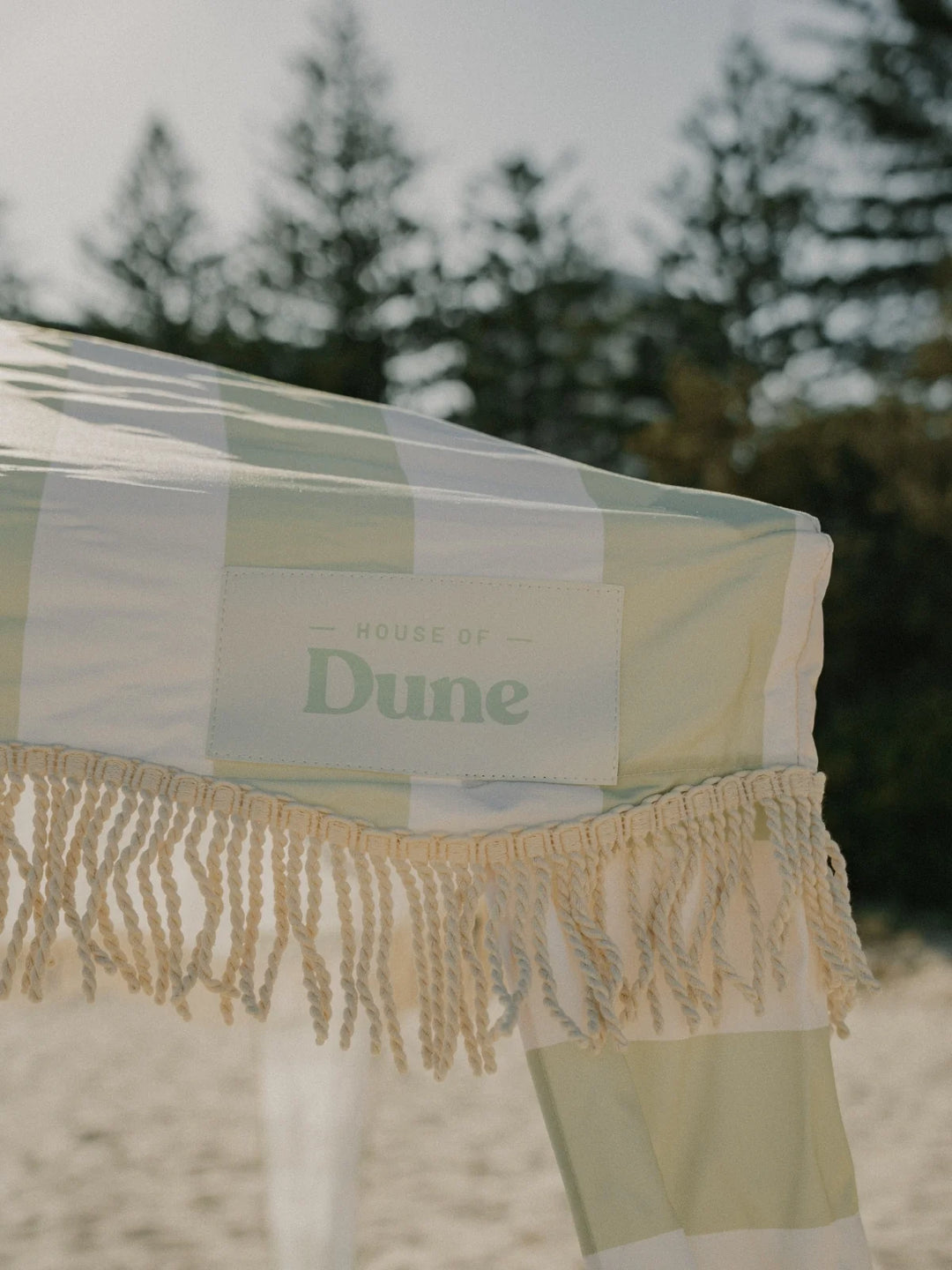 Close-up of the House of Dune Salted Sage Cabana canopy, showcasing the signature green and white stripes, knotted fringe trim, and branded “House of Dune” patch.