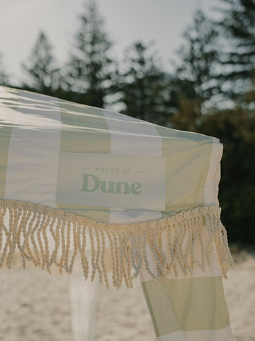 Close-up of the House of Dune Salted Sage Cabana canopy, showcasing the signature green and white stripes, knotted fringe trim, and branded “House of Dune” patch.