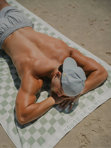 Man wearing grey shorts relaxing face-down on the Salted Sage checkered towel by House of Dune.