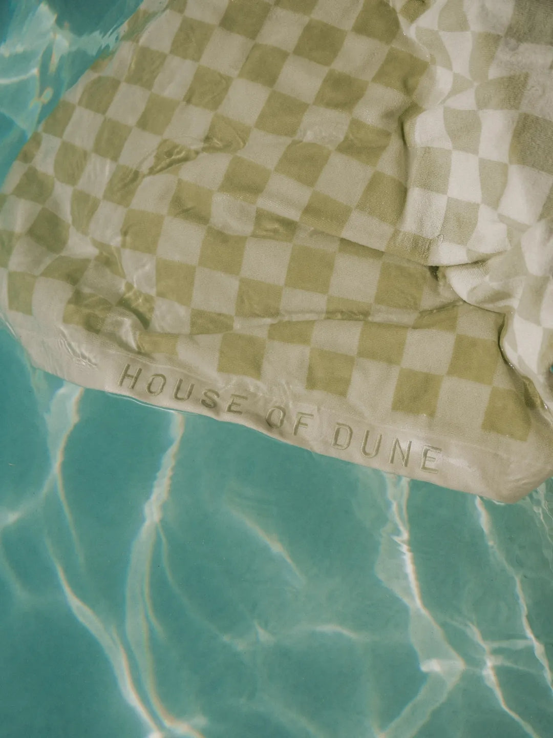 Salted Sage checkered towel by House of Dune partially submerged in turquoise pool water.