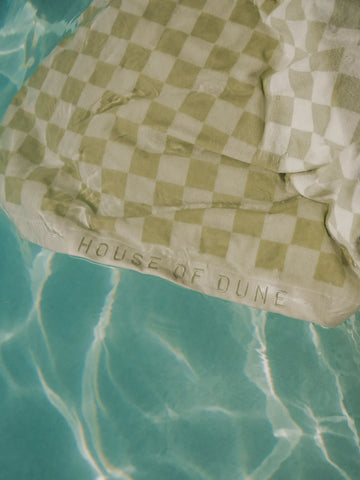 Salted Sage checkered towel by House of Dune partially submerged in turquoise pool water.