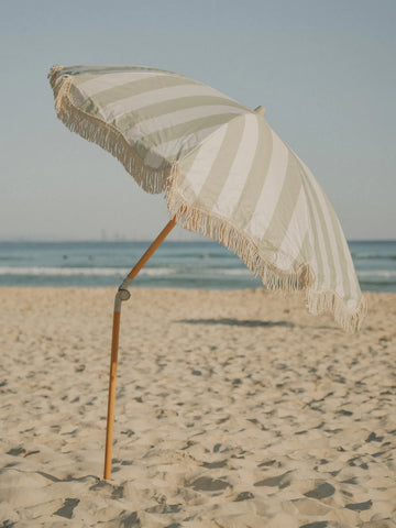 Salted Sage beach umbrella tilted in warm sunlight with subtle sage and white stripes, House of Dune coastal collection.