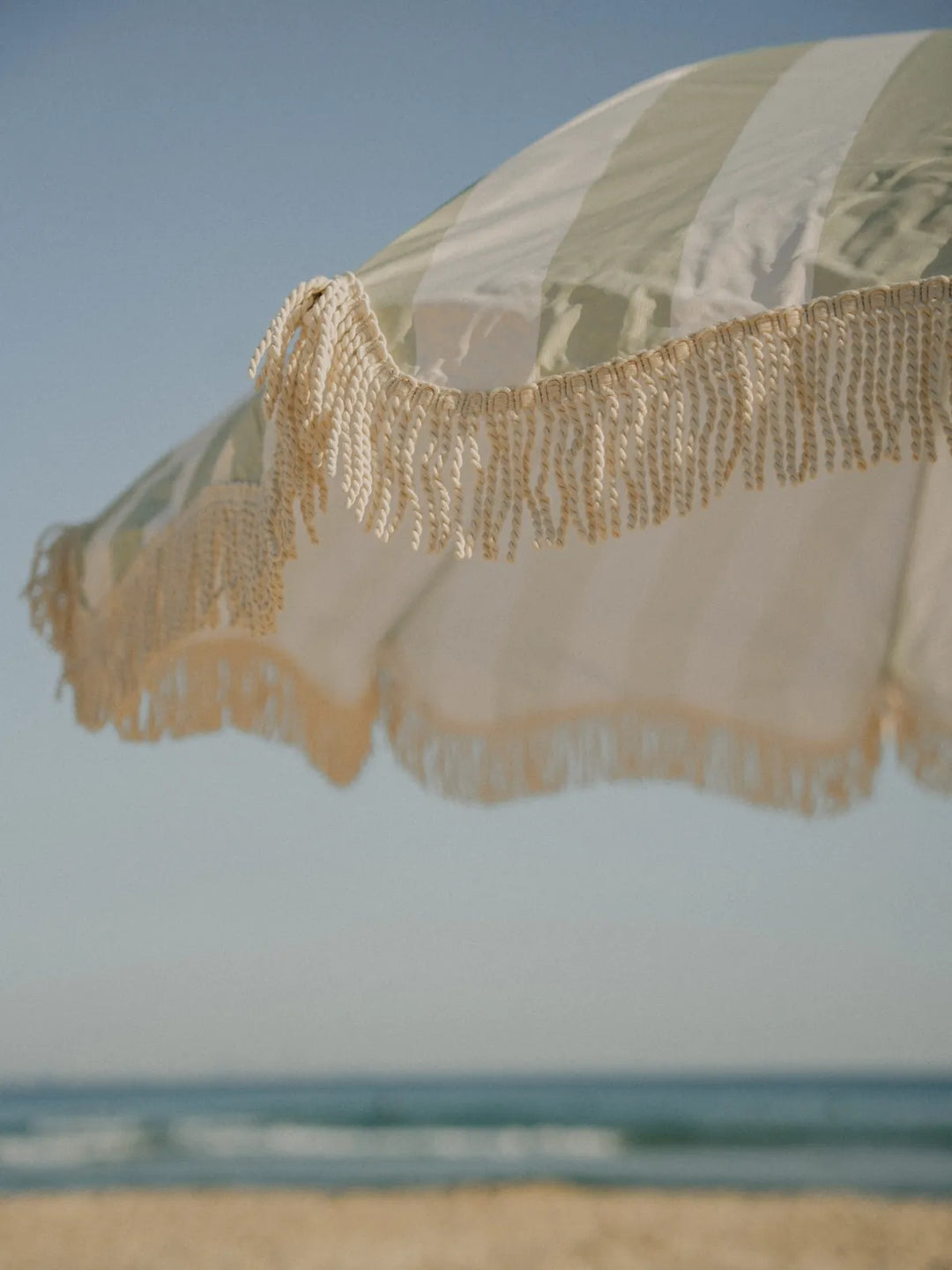 Close-up of the Salted Sage beach umbrella fringe swaying in the coastal breeze by House of Dune.
