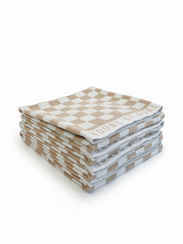 Stack of four House of Dune Sand Drift beach towels featuring a soft beige and white check pattern, folded for a refined coastal look.