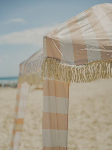 Detail shot of the House of Dune Sand Drift Cabana with wide neutral stripes and knotted fringe, capturing the soft coastal tones of the beach setting.
