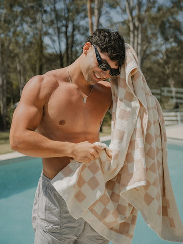 Man drying himself poolside with a Sand Drift checkered towel, wearing sunglasses and shorts, House of Dune.