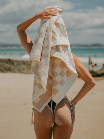 Back view of woman drying her hair with a Sand Drift checkered towel by the ocean, House of Dune coastal collection.