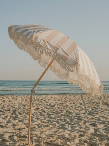 Sand Drift beach umbrella tilted toward the sea, showing neutral stripes and fringe by House of Dune.