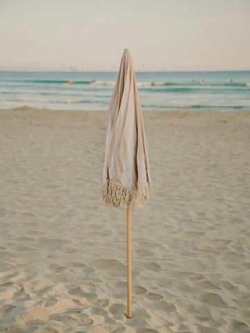 Sand Drift beach umbrella folded upright in the sand with ocean waves in the background, by House of Dune.