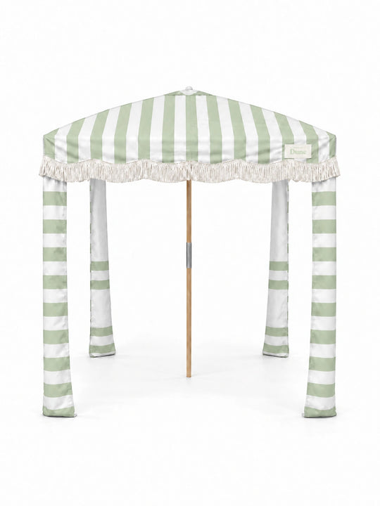 House of Dune Salted Sage beach cabana, front view on white: sage and white striped canopy, off-white fringe, upright striped fabric legs and a wooden centre pole.