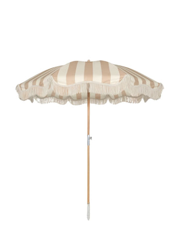 Upright Sand Drift beach umbrella from House of Dune with neutral beige and cream stripes, wooden pole, and fringe edging.
