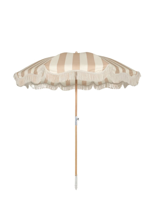 Upright Sand Drift beach umbrella from House of Dune with neutral beige and cream stripes, wooden pole, and fringe edging.