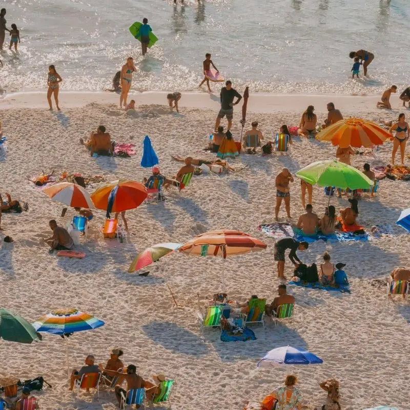 Crowded beach scene with umbrellas and sunbathers, editorial image representing coastal living.