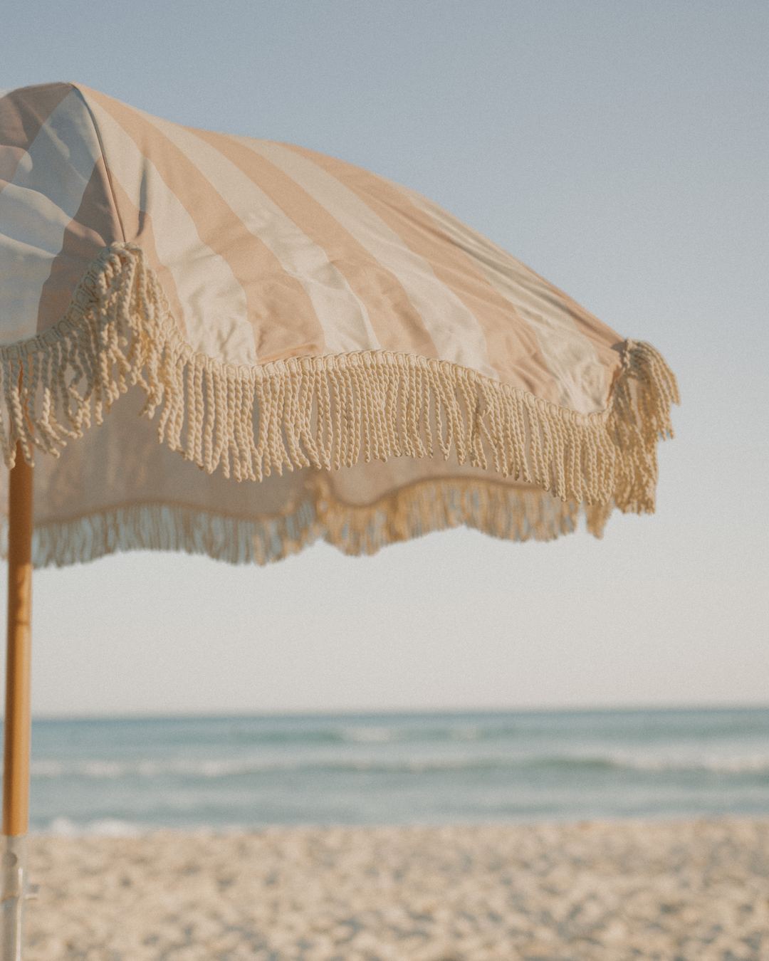 A Beach Umbrella in Sand Drift tilted on the sand, its fringe moving in the breeze
