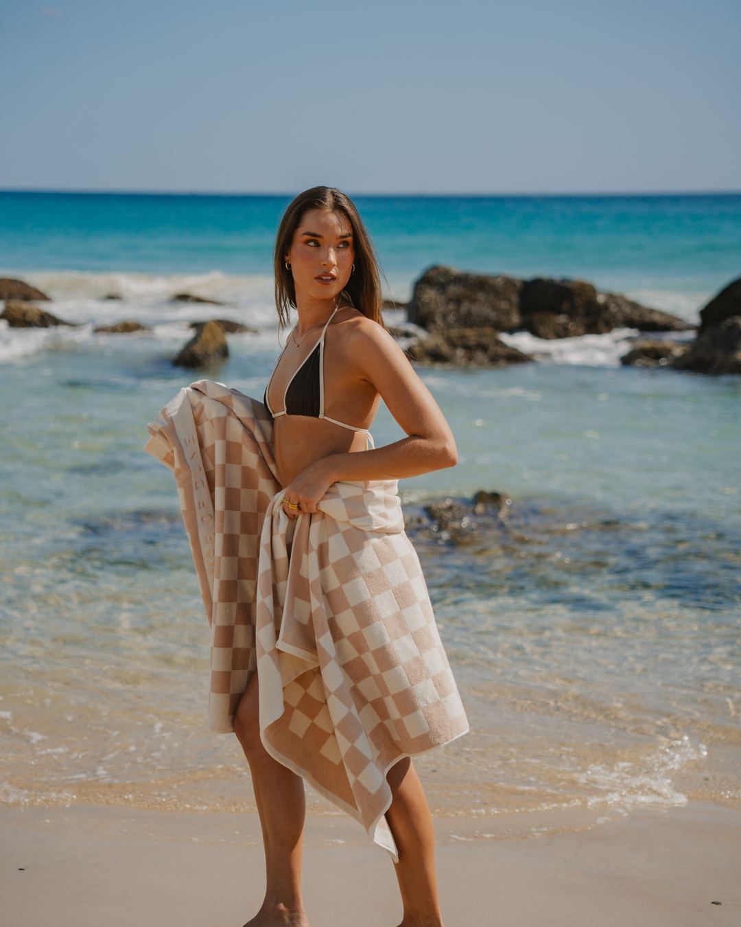 A woman walking out of the shallows with a Sand Drift Beach Towel