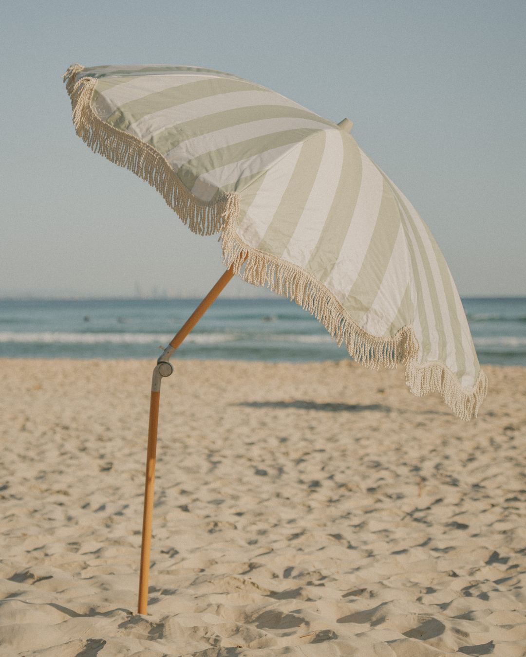 A Salted Sage Beach Umbrella standing alone on an empty beach