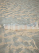 Sand Drift beach umbrella neatly packed in its striped House of Dune carry bag resting on soft sand.