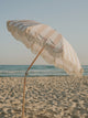 Sand Drift beach umbrella tilted toward the sea, showing neutral stripes and fringe by House of Dune.