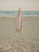 Sand Drift beach umbrella folded upright in the sand with ocean waves in the background, by House of Dune.