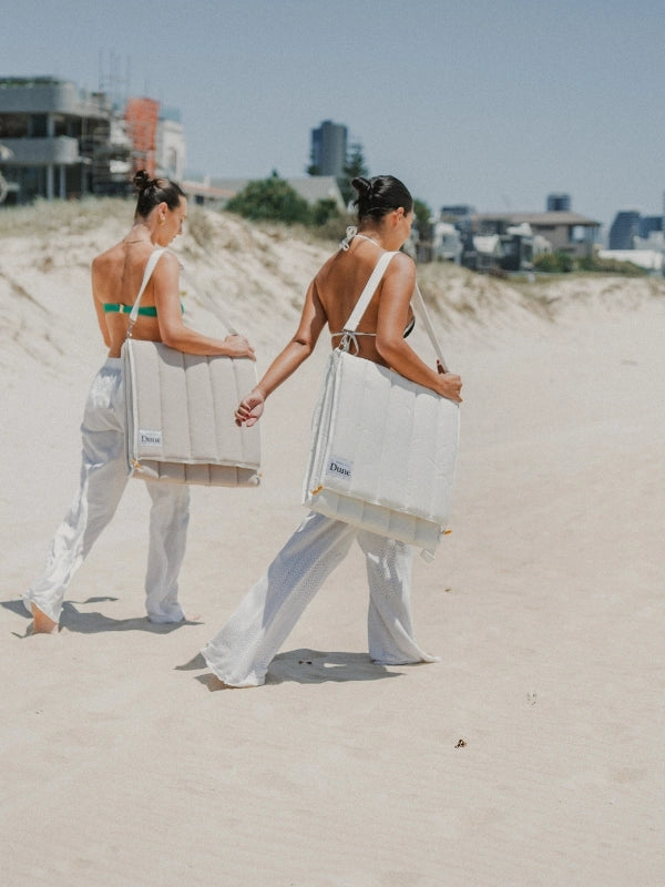 House of Dune beach loungers in Oyster Tide and Sand Drift colours, made from recycled RPET, carried hands-free across coastal sand dunes in foldable backpack style.