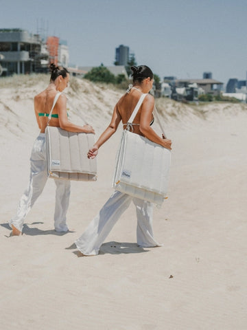 House of Dune beach loungers in Oyster Tide and Sand Drift colours, made from recycled RPET, carried hands-free across coastal sand dunes in foldable backpack style.