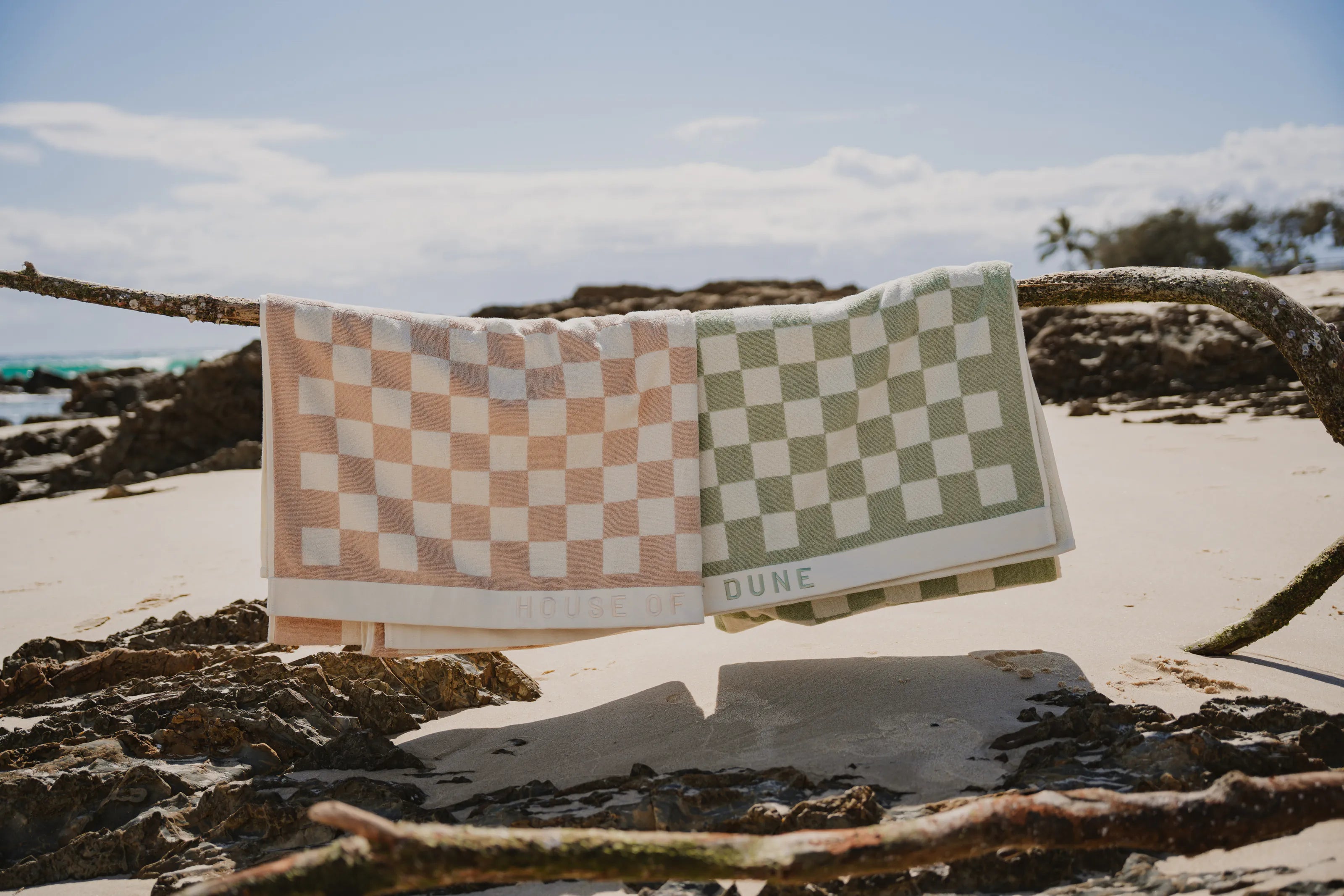 Sand Drift and Salted Sage checked beach towels hanging over driftwood on the beach