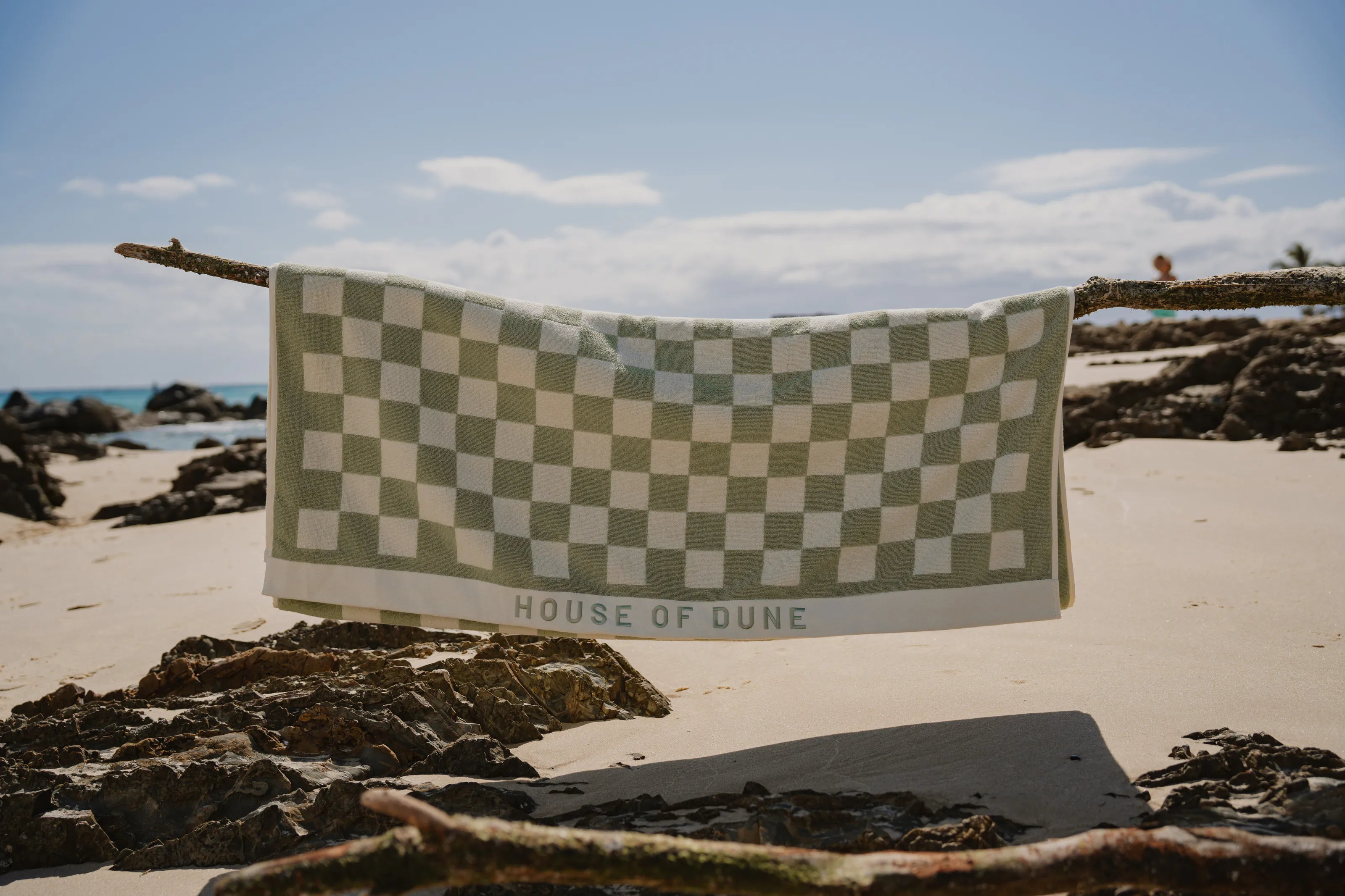 A Salted Sage checked beach towel hung over driftwood above the rocks