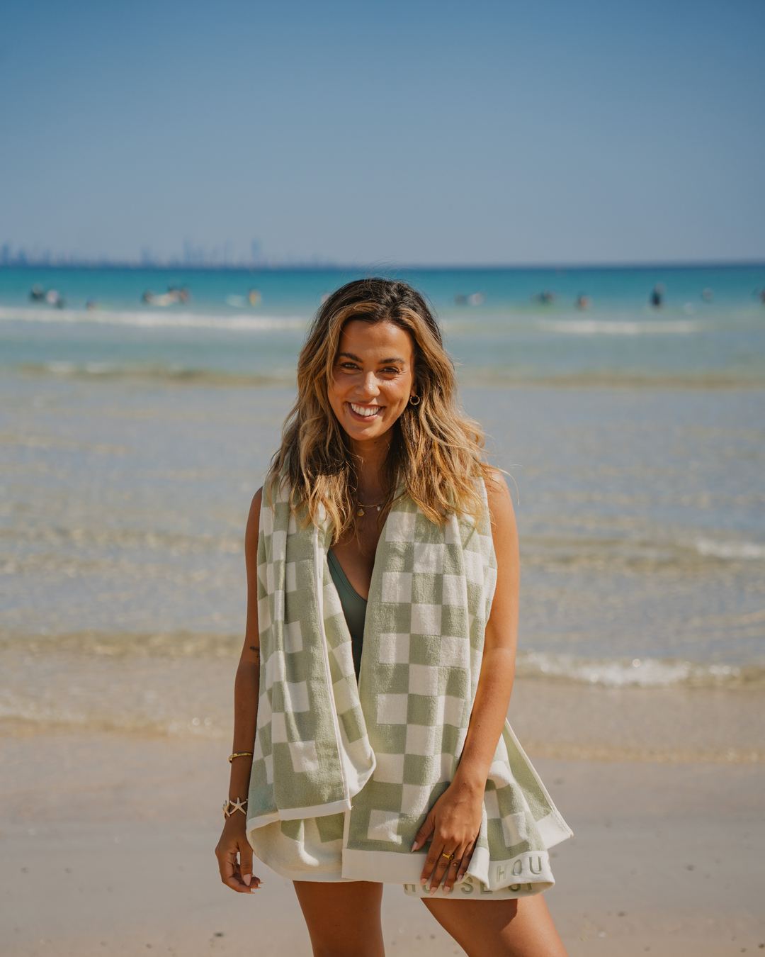 A woman in the shallows with a Salted Sage Beach Towel over her shoulders