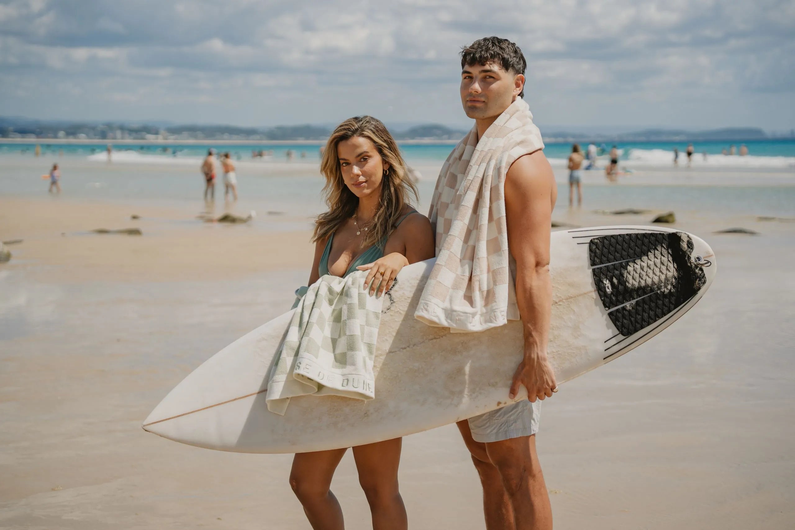 Two friends on the beach with a surfboard and Beach Towels in Sand Drift and Salted Sage