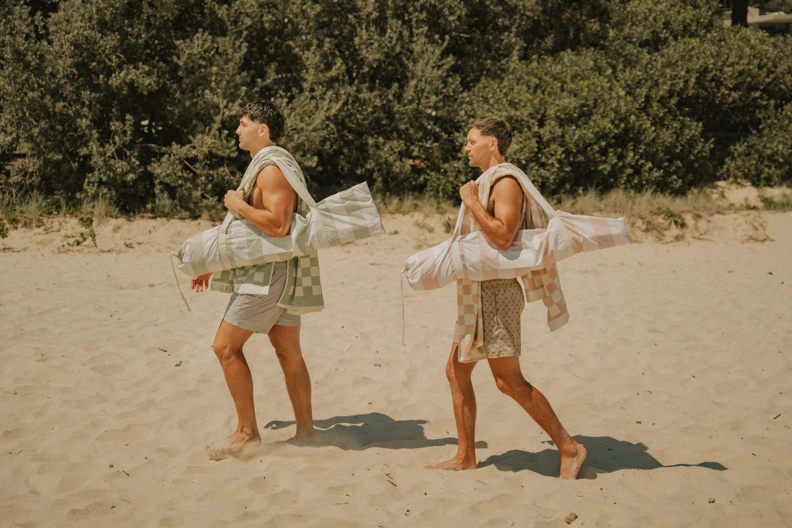 Two friends walking up the beach carrying their beach gear