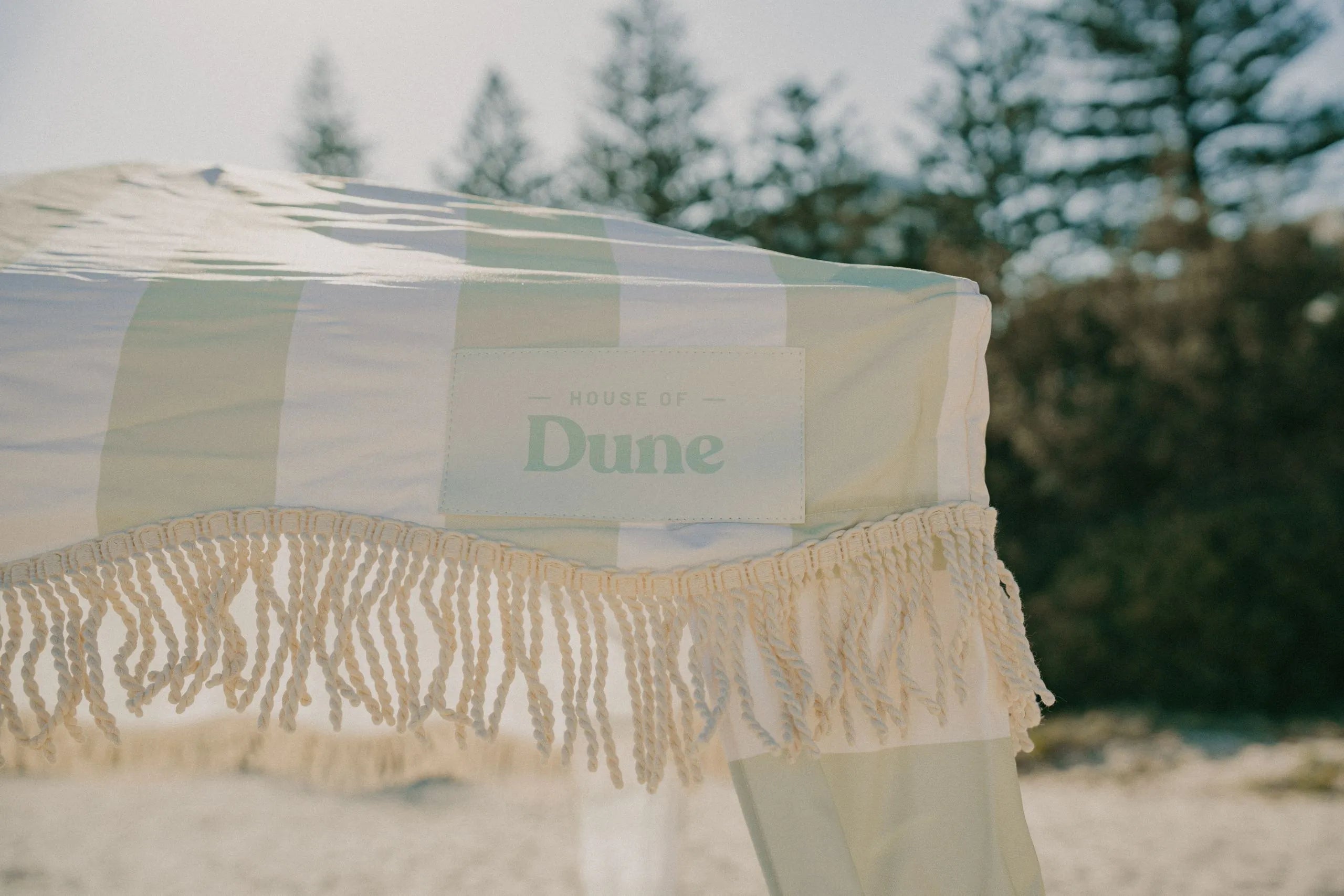 The woven Dune label on the recycled canvas of a Beach Cabana, with pine trees behind