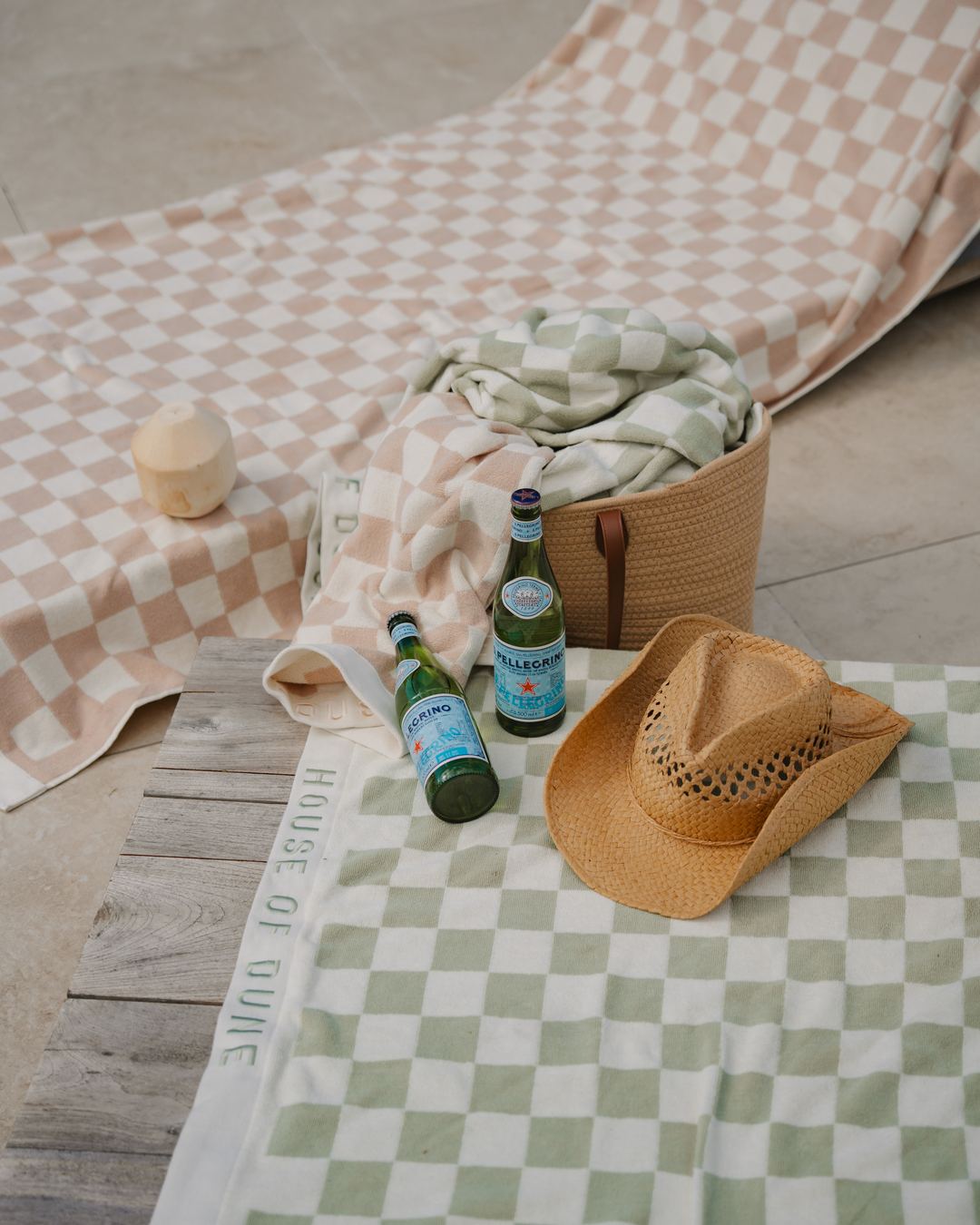 A Salted Sage Beach Towel laid out by a pool with a straw hat and drinks