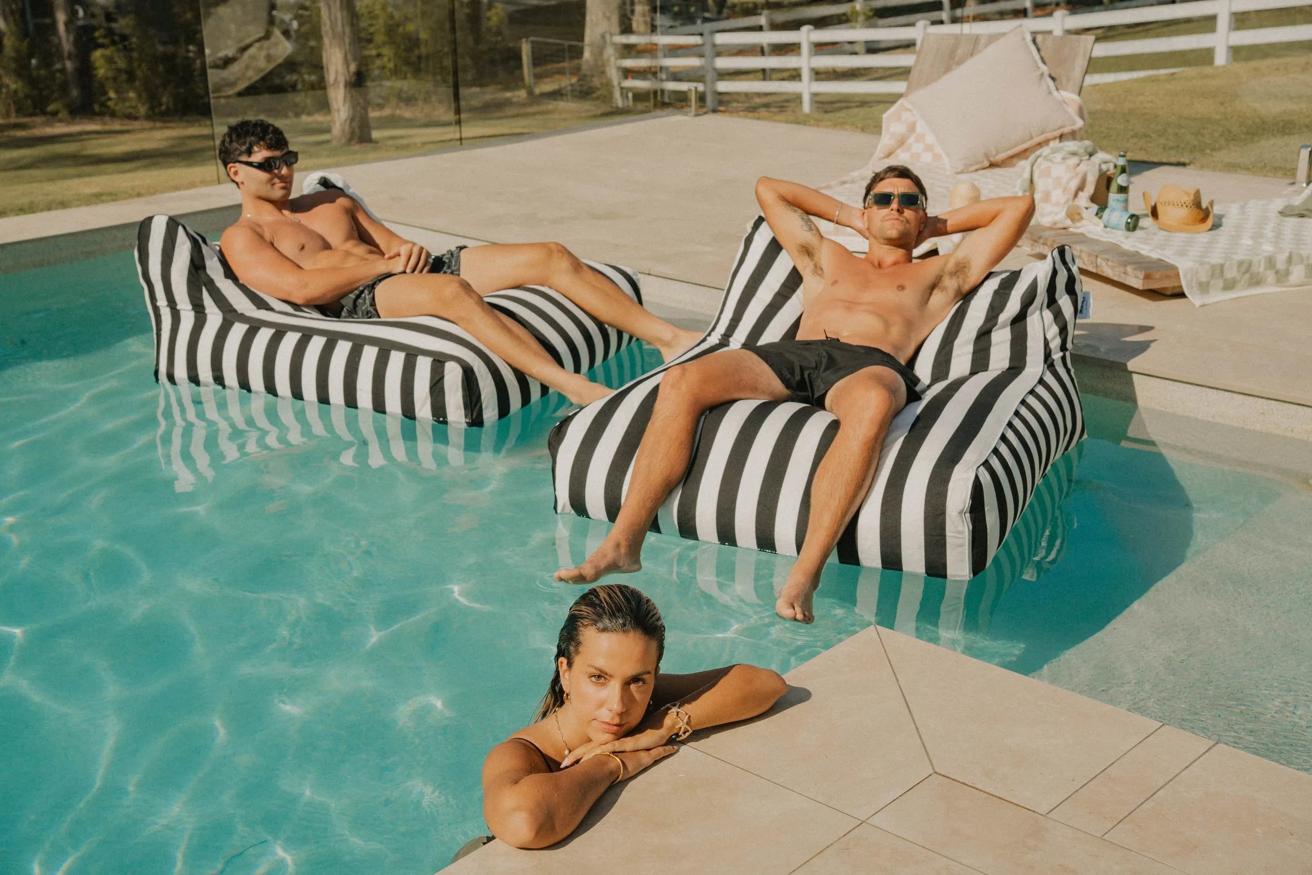 Friends relaxing on striped Floating Loungers in a pool